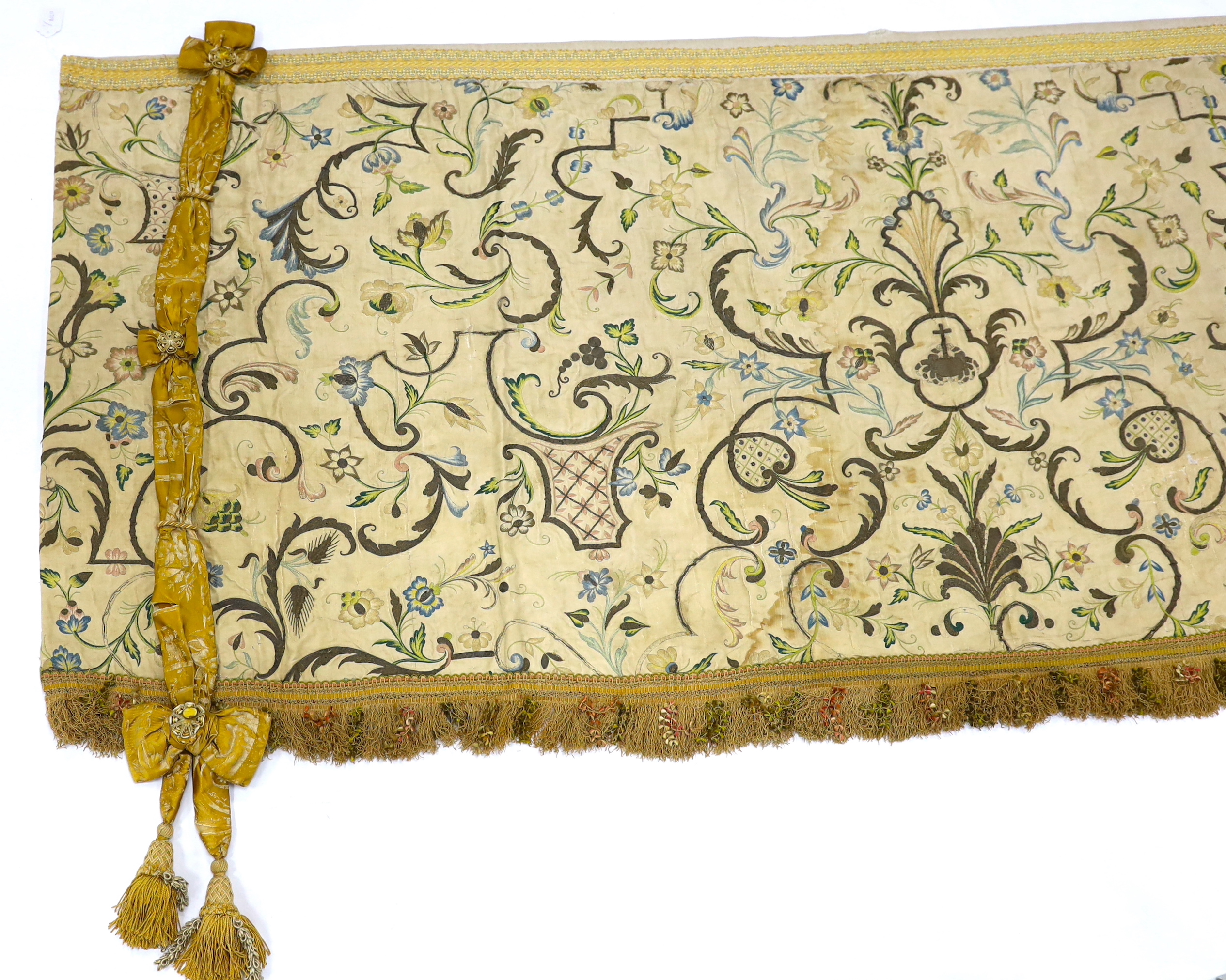 A mid-18th century Continental silk embroidered altar cloth, embroidered with polychrome silks and silver metallic threads in an all-over floral design on cream silk with ornate silk tasselling, (the damask tie backs add